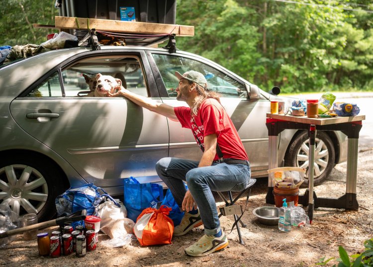 Tyler Asselin, 30, scratches the chin of his dog, Meechy, while his other dog, Penny Lane, peeks out from behind Thursday. Asselin said he has been living in his car since June and has been parked at the David Rancourt Preserve in Lewiston for the last 10 days. He recently had to take a week off from work to be with his dogs full time while Penny was under quarantine for nipping at a child who startled the dog. The Lewiston native and former Leavitt Area High School student said he keeps himself busy at the preserve by picking up trash and collecting broken glass from the paths.